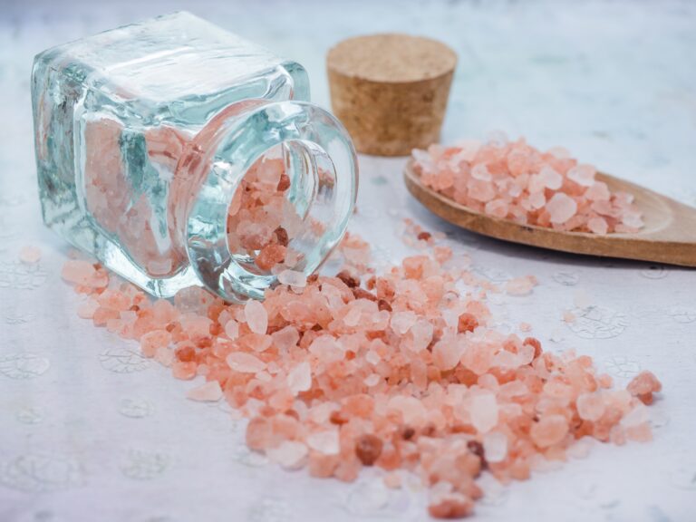 A closeup shot of a jar and a wooden spoon with pink sea salt